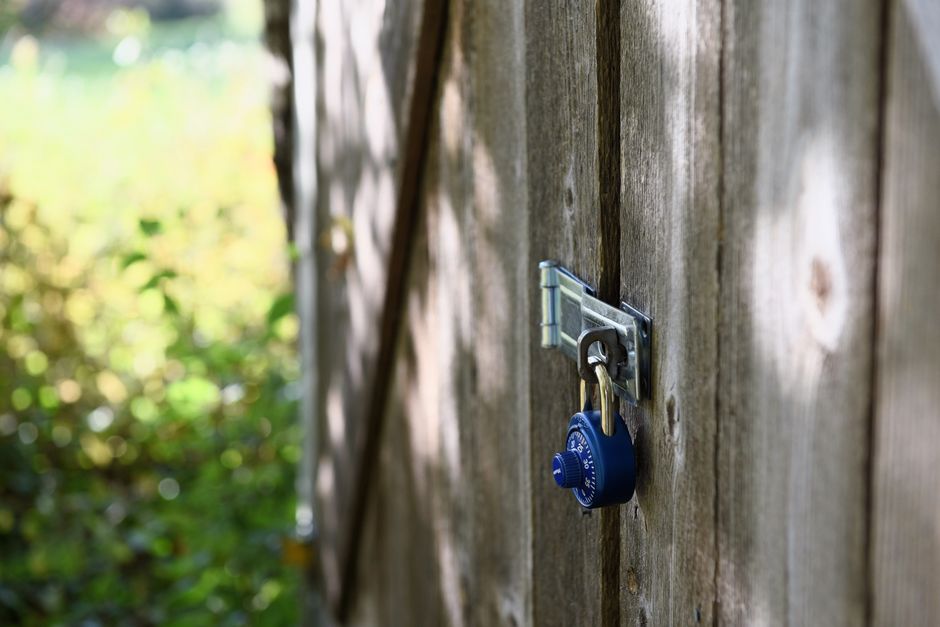 A blue padlock secures a wooden gate outdoors with sunlight filtering through.